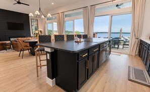 Una cocina moderna con una isla grande, zona de comedor con sofá y sillas, y vista al lago.