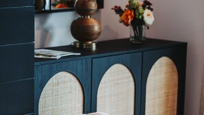 Una cesta de mimbre con un tejido de punto, una lámpara y un florero con flores sobre un mueble oscuro.