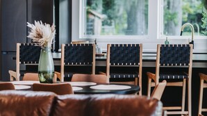 Una cocina moderna con muebles oscuros, un comedor con sillas de madera y una mesa, y vistas al exterior con vegetación.