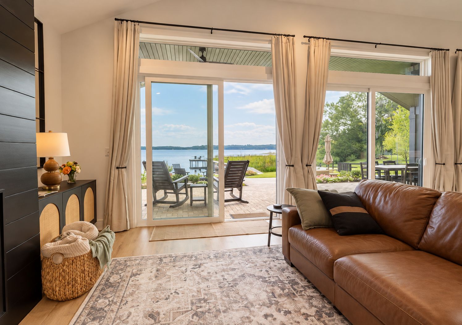 Una habitación con sofá de cuero, una cesta tejida, una lámpara y vistas a un espacio de estar exterior junto al agua.