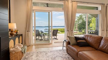 Una habitación con sofá de cuero, una cesta tejida, una lámpara y vistas a un espacio de estar exterior junto al agua.