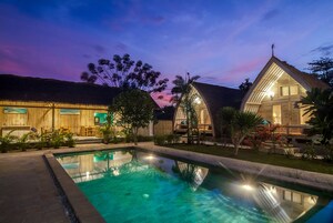 A pool area with a clear pool, wooden buildings, and a sunset sky.