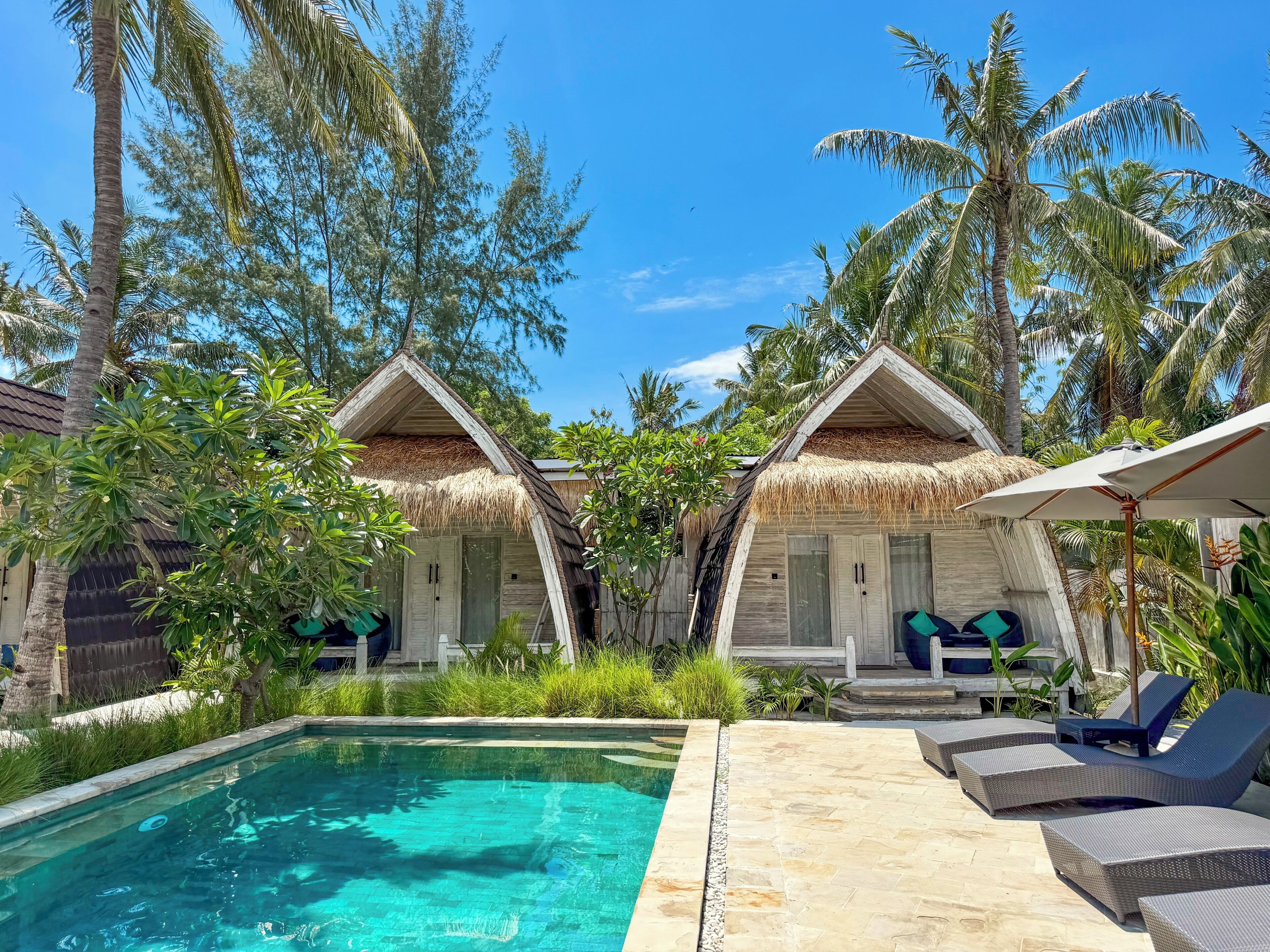 Un espace aménagé au bord de la piscine, comprenant deux petits chalets à toits de chaume, des chaises longues et une piscine à eau cristalline.