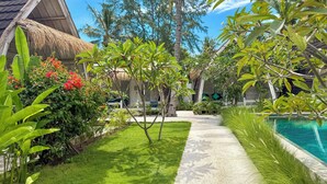 A tropical resort with a thatched-roof building, a swimming pool, and lush greenery. - Gili Air Escape - Adults Only (Gili Air)