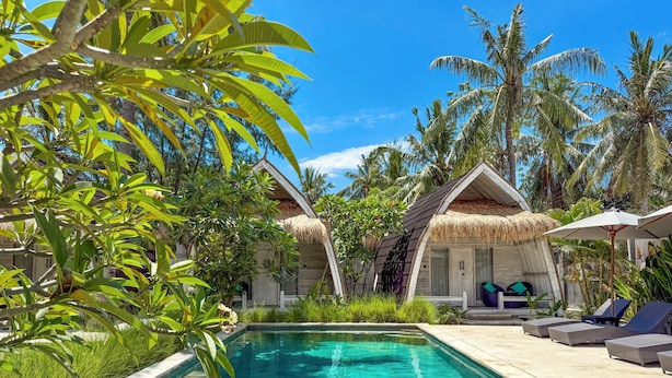 A poolside area with a clear pool, lounge chairs, and thatched-roof structures. - Gili Air Escape - Adults Only (Gili Air)