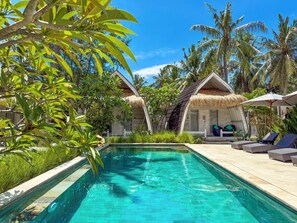 A poolside area with a clear pool, lounge chairs, and thatched-roof structures. - Gili Air Escape - Adults Only (Gili Air)