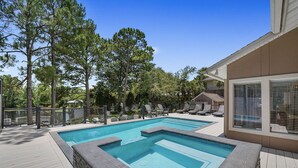A rectangular swimming pool with a stone border, surrounded by a wooden deck and lounge chairs. - Shell Mates - Luxury Lakefront Vacation Rental with Private Pool Space & Outdoor Area (Miramar Beach)