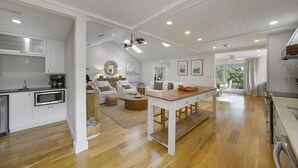 A spacious kitchen with white cabinetry, a wooden dining table, and a seating area with a sofa and chairs. - Shell Mates - Luxury Lakefront Vacation Rental with Private Pool Space & Outdoor Area (Miramar Beach)