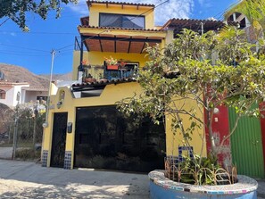 A two-story building with a garage, a balcony with potted plants, and a tree in the foreground.