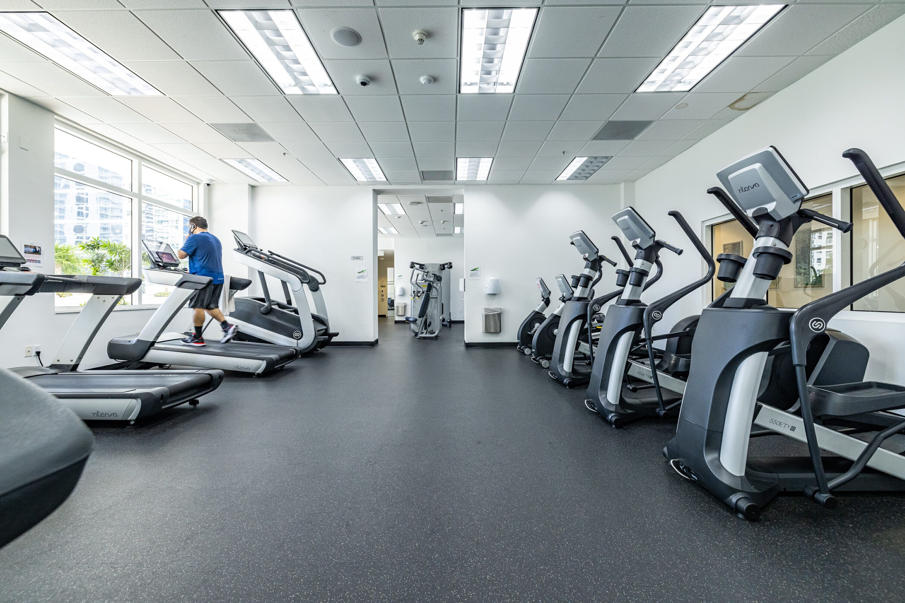A gym with treadmills, elliptical machines, and a person using a treadmill.