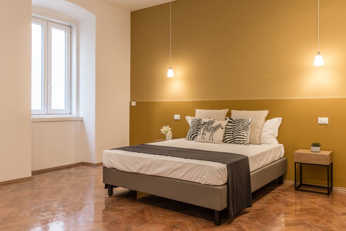 Un dormitorio con una cama, mesitas de noche, una ventana y una lámpara de pared.
