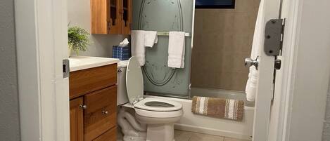 A bathroom with a toilet, a wooden cabinet, a towel rack, and a shower area.