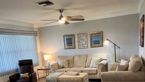 A living room with a sofa, ottoman, and chair, a ceiling fan, and a floor lamp.