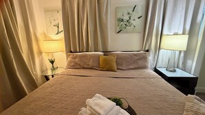 A neatly made bed with a textured blanket, a small bedside table with a lamp, and a vase with flowers. - Suarez art stay Private Rooms at Miami Centrally Located with free Parking (Miami)
