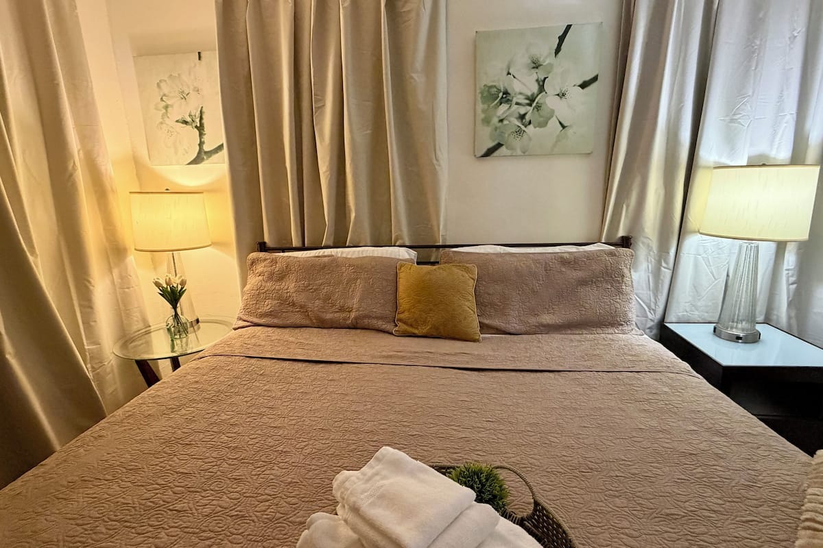 A neatly made bed with a textured blanket, a small bedside table with a lamp, and a vase with flowers.