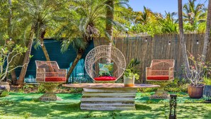 A tropical outdoor seating area with wicker chairs and a round wicker swing, surrounded by lush greenery and a bamboo fence. - Suarez art stay Private Rooms at Miami Centrally Located with free Parking (Miami)