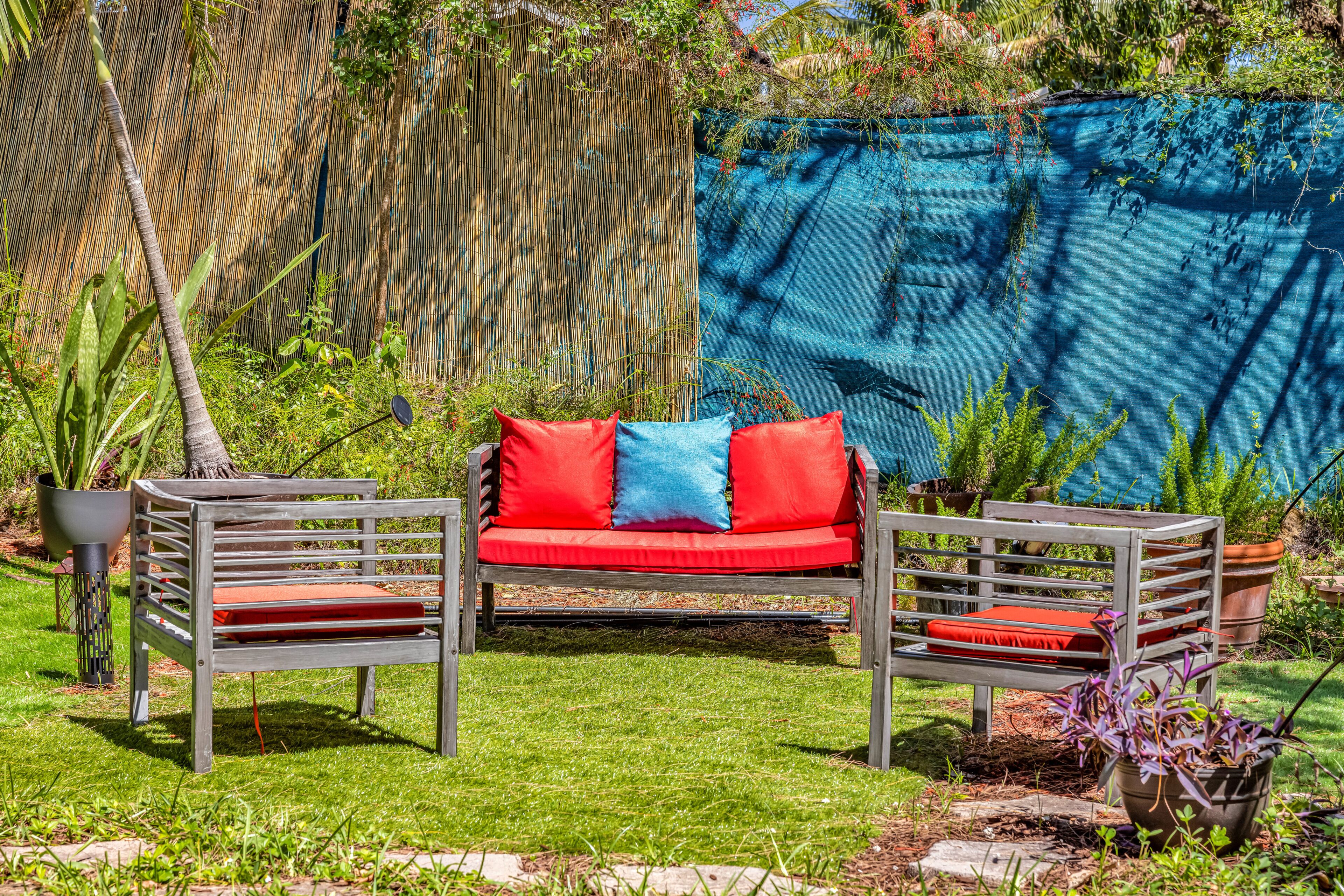 A garden with a red sofa and two chairs, surrounded by plants and a bamboo fence.