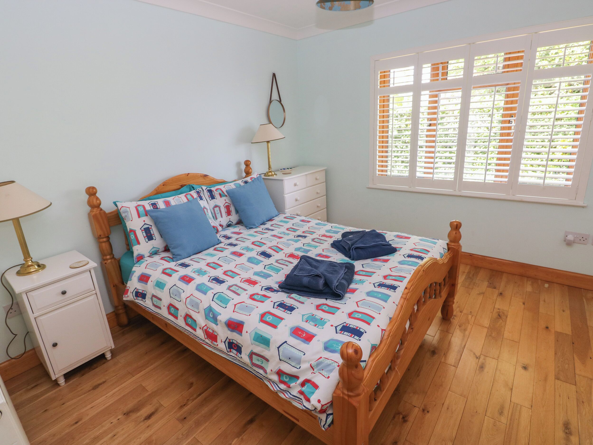 A bedroom with a wooden bed, a nightstand, a lamp, and a window with blinds.