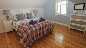 A bedroom with a bed, two bedside tables, a nightstand, a dresser, a window, and a hanging light fixture. - Yr Hen Ardd (Haverfordwest)