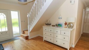 A spacious room with a wooden floor, a white staircase, a white dresser with drawers, and a door leading outside. - Yr Hen Ardd (Haverfordwest)