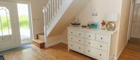 A spacious room with a wooden floor, a white staircase, a white dresser with drawers, and a door leading outside.