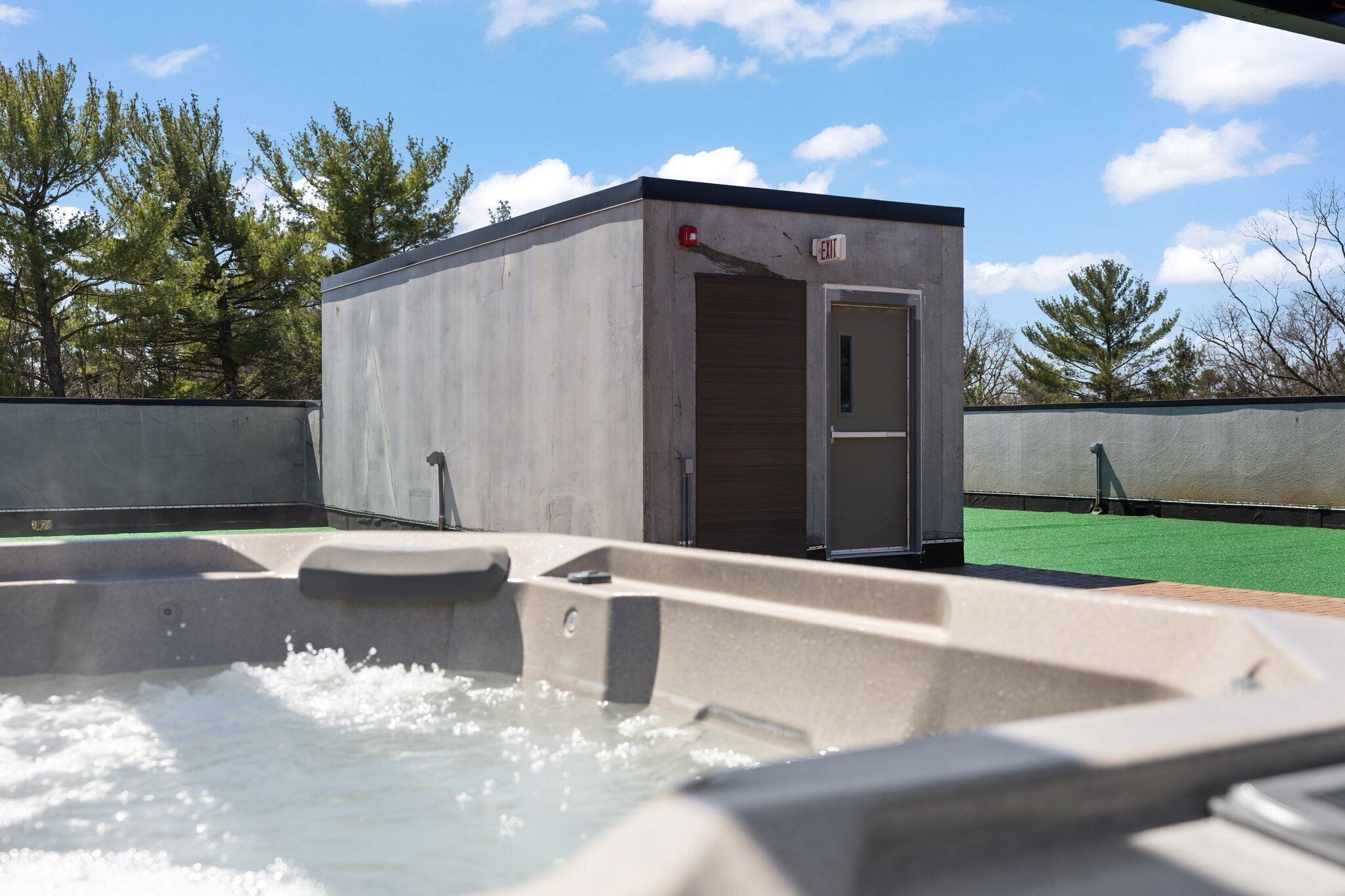 A hot tub with a small adjacent structure, possibly a changing room, and a green artificial turf area in the background.