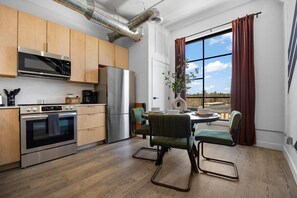 A modern kitchen with stainless steel appliances, wooden cabinets, and a dining area with green chairs.