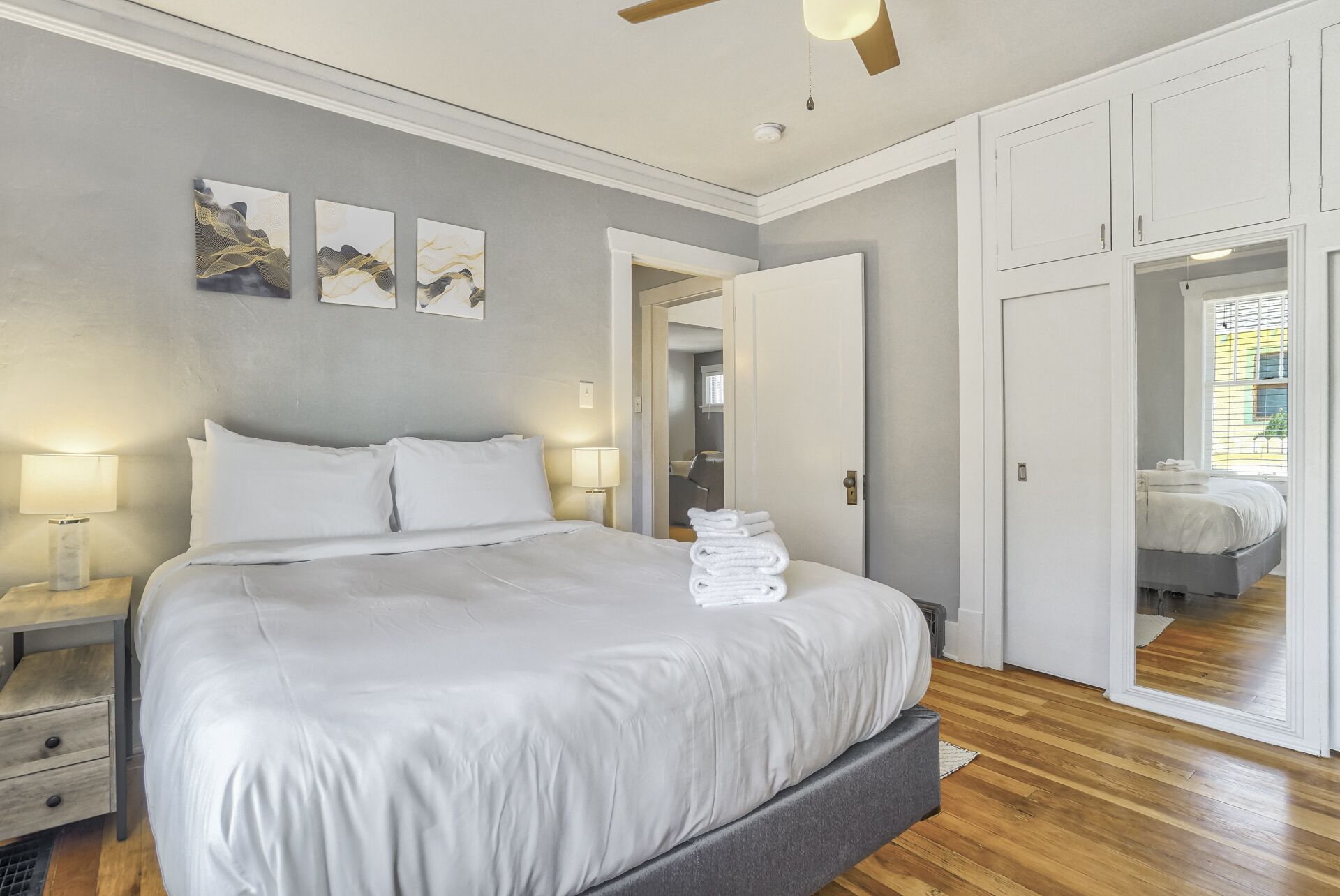 A bedroom with a bed, bedside lamps, a ceiling fan, and a view into the bathroom through an open door.