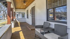 Une véranda couverte avec un plancher en bois, des meubles en osier et de grandes fenêtres.