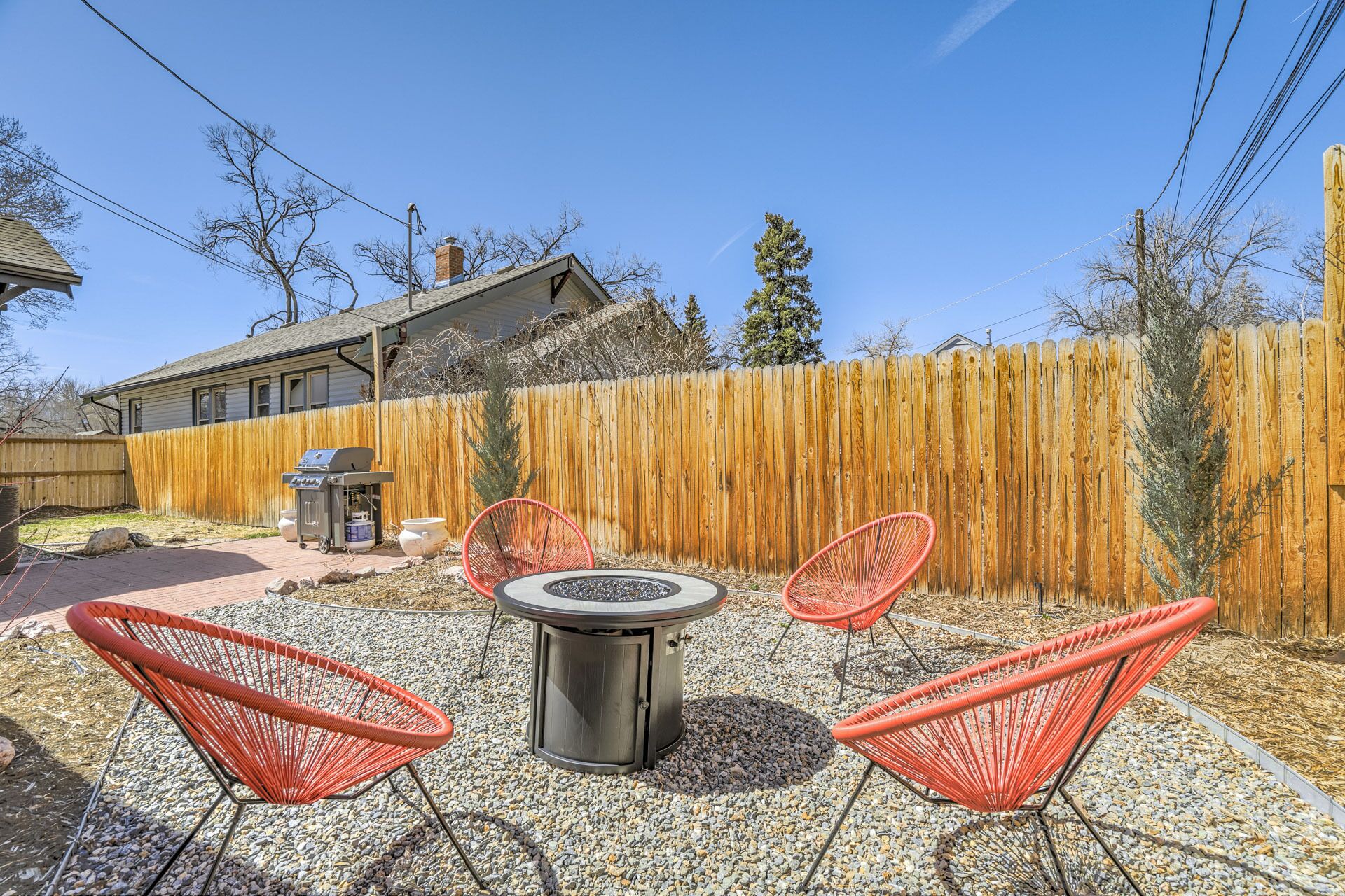Un jardin avec un barbecue, un foyer et des chaises rouges.