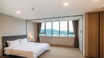 Habitación de hotel con cama, ventana con cortinas, armario de madera y vistas a un paisaje montañoso.