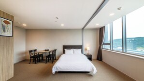 A hotel room with a large bed, a desk with chairs, a window with a view, and a painting on the wall.