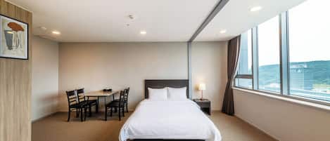 Quarto de hotel com uma cama grande, uma escrivaninha com cadeiras, uma janela com vista e um quadro na parede.