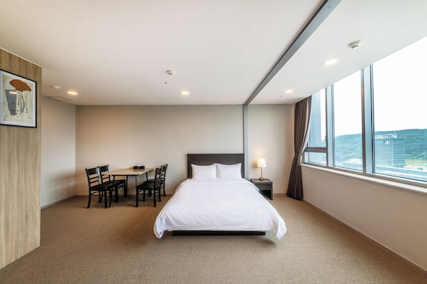 A hotel room with a large bed, a desk with chairs, a window with a view, and a painting on the wall.