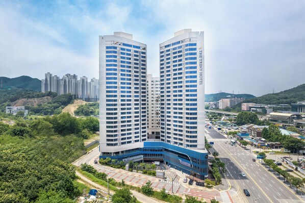 A high-rise hotel with a curved blue entrance, surrounded by greenery and a busy road. - The Triny Urban Suites (Yongin)
