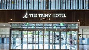 The entrance of The Triny Hotel with a modern design, featuring glass doors and a sign above.