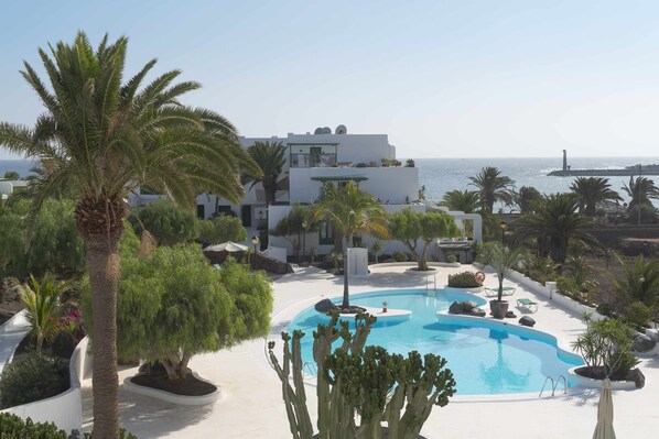 Zona de piscina con vista despejada al mar, rodeada de palmeras y un edificio moderno.