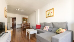Un salon avec un canapé gris, une table basse blanche et une table à manger en bois, accompagnée de chaises.