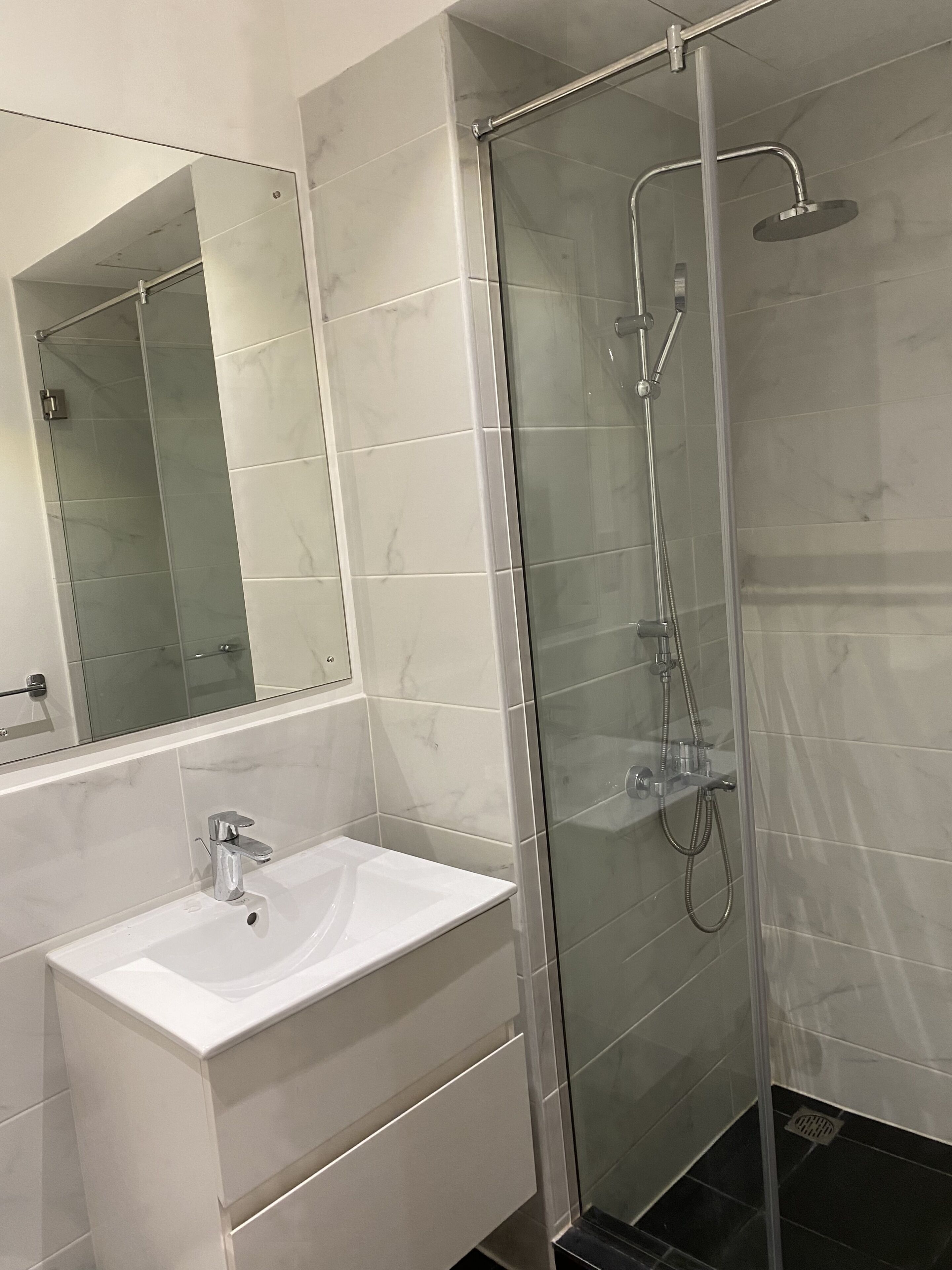 Un bagno moderno con cabina doccia in vetro, un lavandino bianco e uno specchio grande.