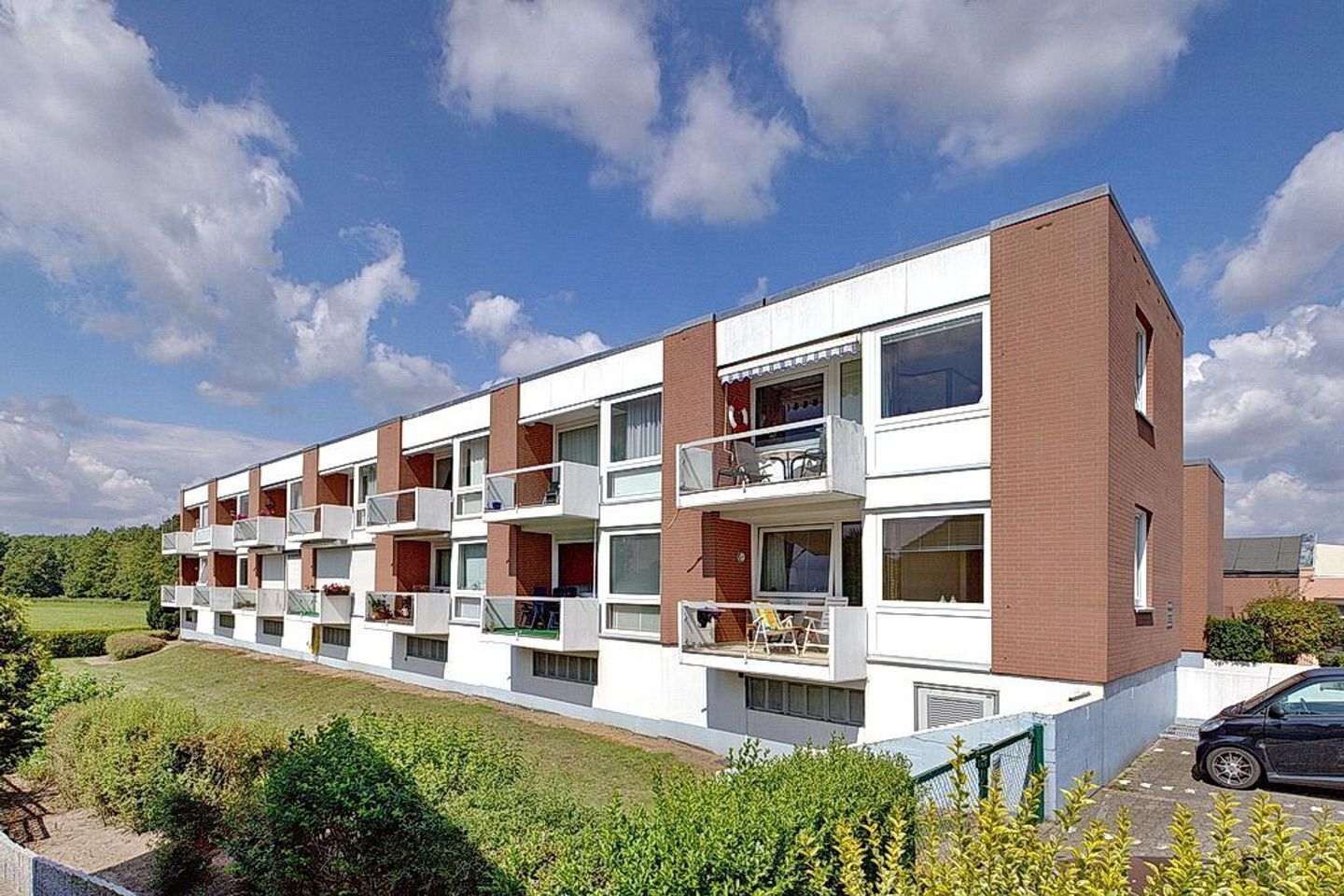 Un edificio de varios pisos con balcones, zona de estacionamiento y paisaje con césped.