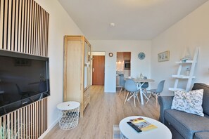 En moderne stue med et fladskærms-tv, en sofa, et sofabord og et spiseområde med stole.