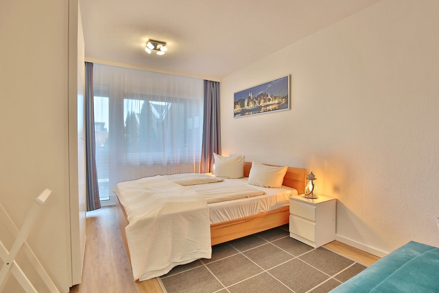 A neatly arranged bedroom with a bed, bedside table, and a cityscape painting on the wall.