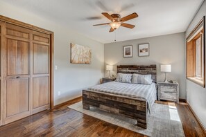 A bedroom with a wooden bed, a ceiling fan, two bedside tables with lamps, and a large window. - Bakers Creek (Woodland Park)