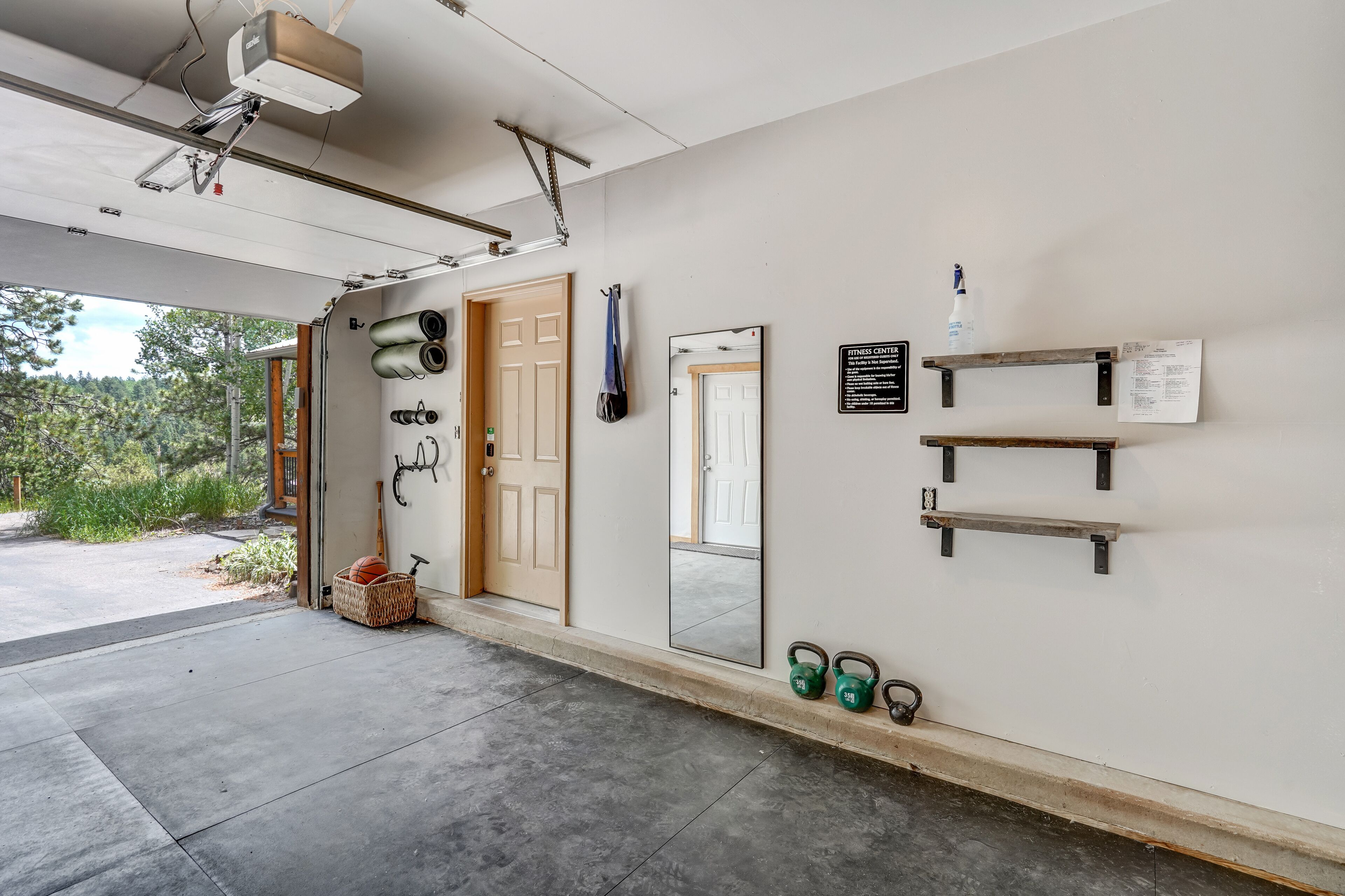 A clean, well-organized garage with a door leading to a driveway, a mounted projector, exercise equipment, and a mirror on the wall.