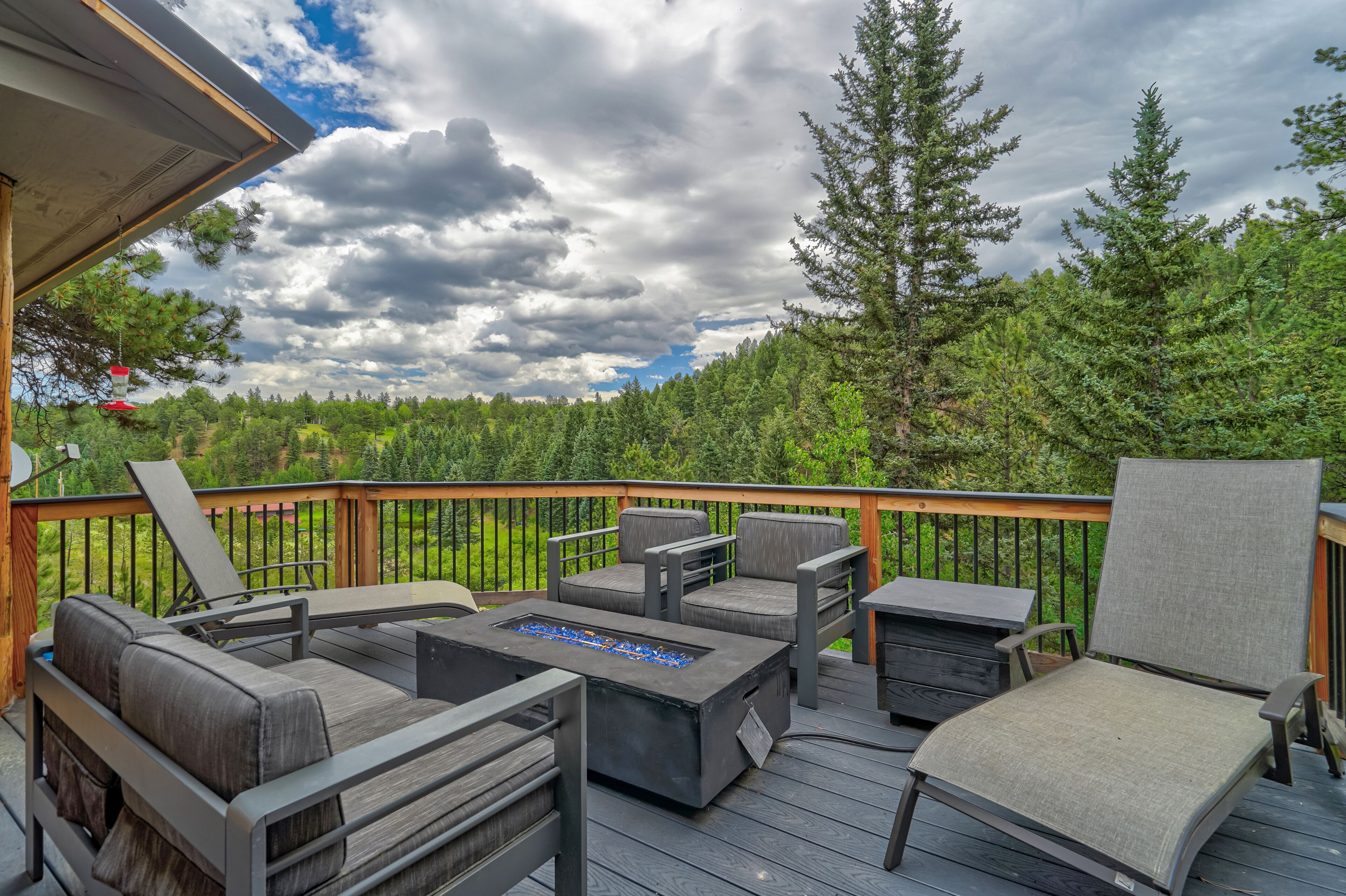 A deck with outdoor furniture, including a sofa, chairs, and a table with a built-in fire pit.