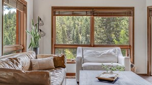 A room with a large window, a sofa, a chair, and a coffee table. - Bakers Creek (Woodland Park)