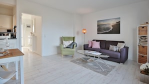 A modern living room with a sofa, armchair, coffee table, and a dining area with a table and chairs.