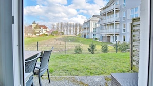 A view from a balcony with a grassy yard, a fence, and a building with multiple balconies.