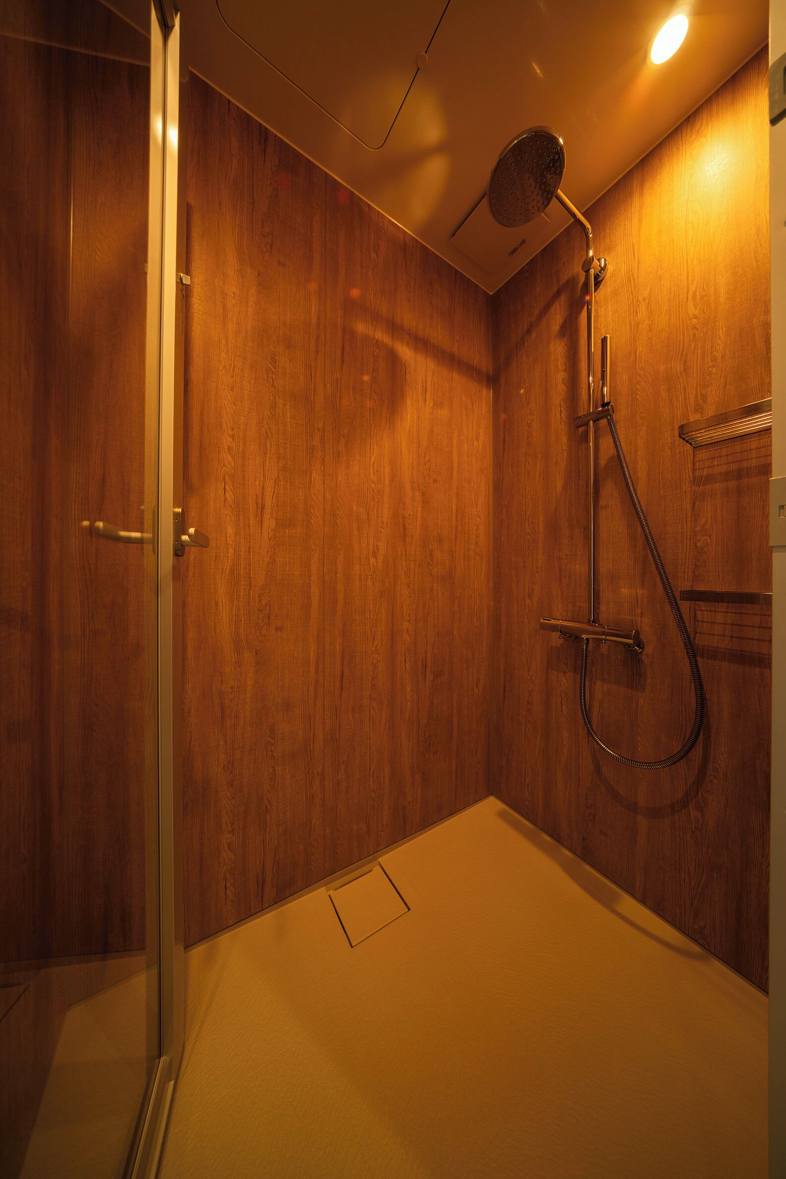 A wooden-paneled shower room with a glass door, a handheld showerhead, and a wall-mounted towel rack.
