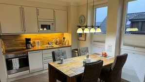 Uma cozinha moderna com mesa de madeira, quatro cadeiras, micro-ondas e cafeteira.